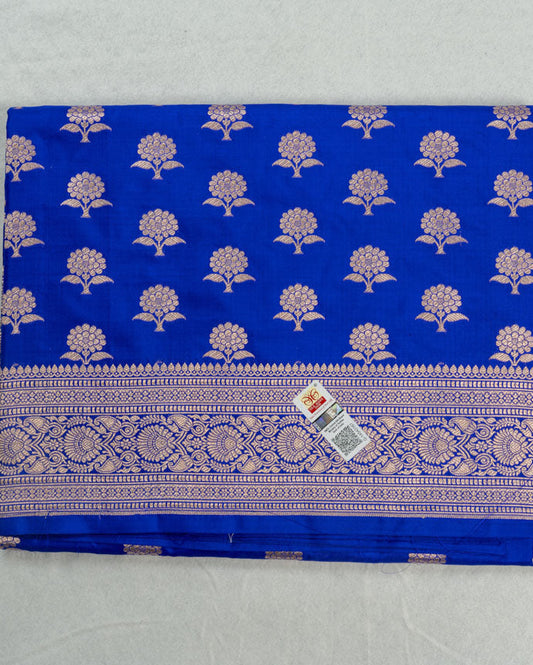 A folded royal blue fabric saree or textile piece featuring a silver floral block print pattern and a detailed silver zari border, with a small price tag attached.