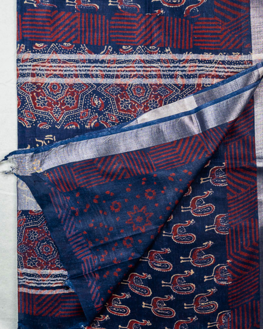 A folded and draped blue patterned cotton shawl or scarf with red and cream motifs, shown against a light background with a brand logo and text at the bottom.