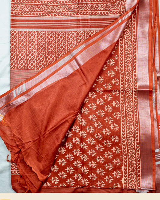 A folded and draped rust orange pure linen cotton sari with white floral and geometric block prints, displayed on a light background with a brand logo banner at the bottom.